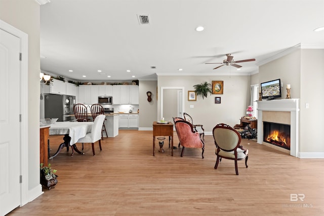 dining space featuring a glass covered fireplace, visible vents, ornamental molding, and light wood finished floors