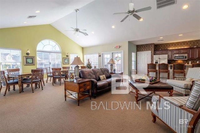 living area with light colored carpet, a ceiling fan, visible vents, and high vaulted ceiling