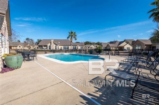 community pool with a patio, fence, and a residential view