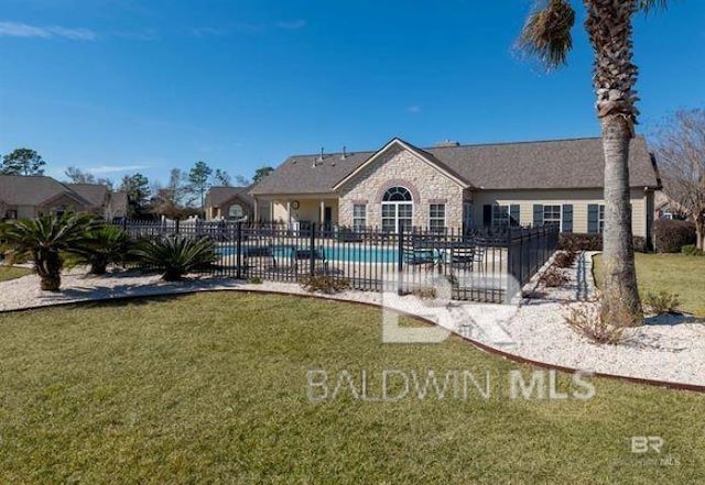 rear view of property with a yard, fence, a fenced in pool, and stone siding