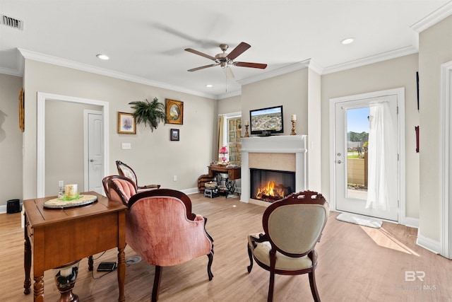 living room featuring light wood-type flooring, visible vents, ornamental molding, a tiled fireplace, and ceiling fan