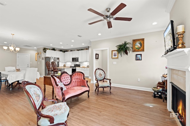 living area featuring light wood finished floors, ceiling fan with notable chandelier, a tile fireplace, and ornamental molding