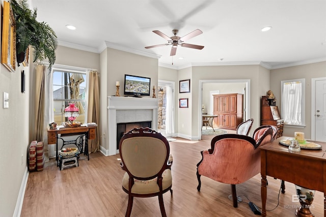 living area with a tiled fireplace, crown molding, light wood-type flooring, and ceiling fan