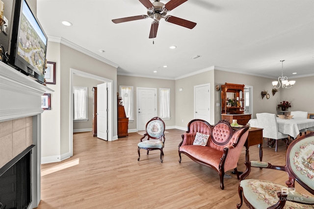 living area featuring a wealth of natural light, ceiling fan with notable chandelier, a fireplace, and light wood-type flooring