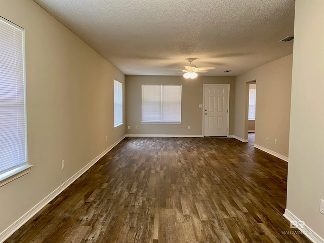 empty room with a healthy amount of sunlight, ceiling fan, dark wood-type flooring, and a textured ceiling