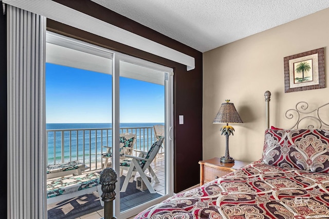 bedroom with a textured ceiling, access to outside, a water view, and a view of the beach