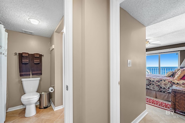 bathroom featuring a textured ceiling, a water view, toilet, and baseboards