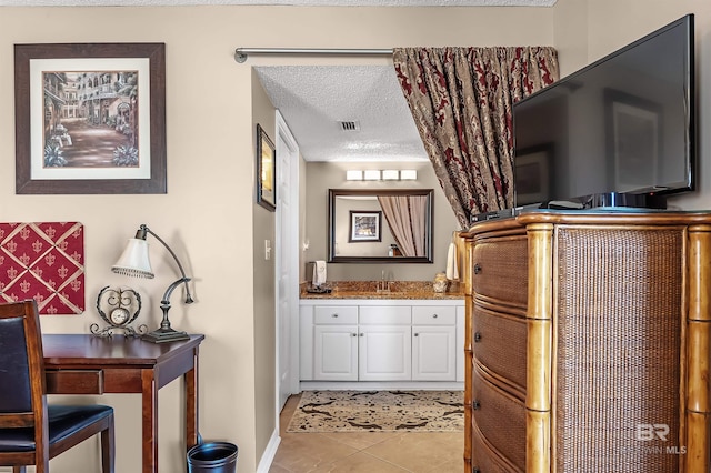 interior space featuring tile patterned flooring, visible vents, a textured ceiling, and vanity