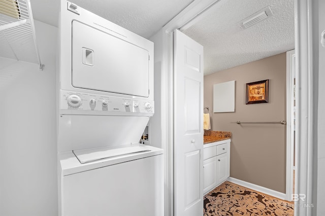 laundry room with laundry area, baseboards, visible vents, stacked washer / dryer, and a textured ceiling