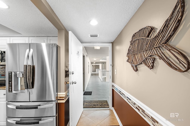 corridor featuring light tile patterned floors, visible vents, and a textured ceiling