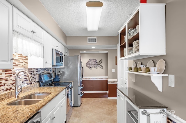 kitchen with light stone counters, stainless steel appliances, a sink, visible vents, and glass insert cabinets