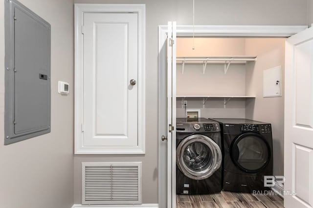 washroom with hardwood / wood-style flooring, electric panel, and washing machine and dryer