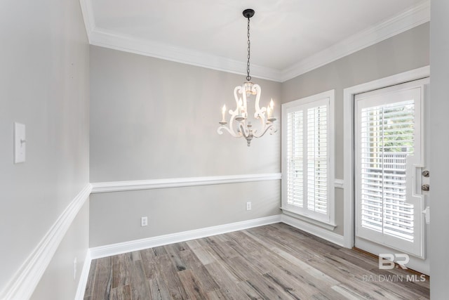 unfurnished dining area featuring light wood-type flooring, crown molding, and an inviting chandelier