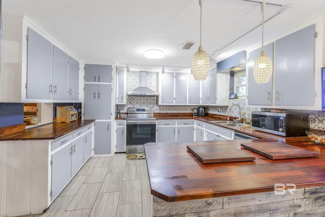 kitchen featuring sink, wooden counters, hanging light fixtures, appliances with stainless steel finishes, and wall chimney range hood