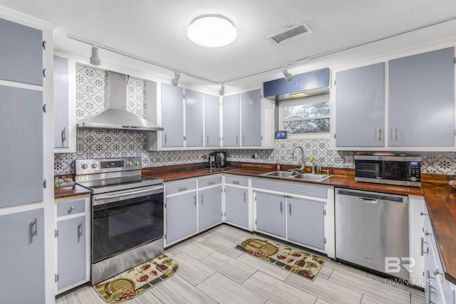 kitchen featuring sink, rail lighting, wooden counters, appliances with stainless steel finishes, and wall chimney exhaust hood