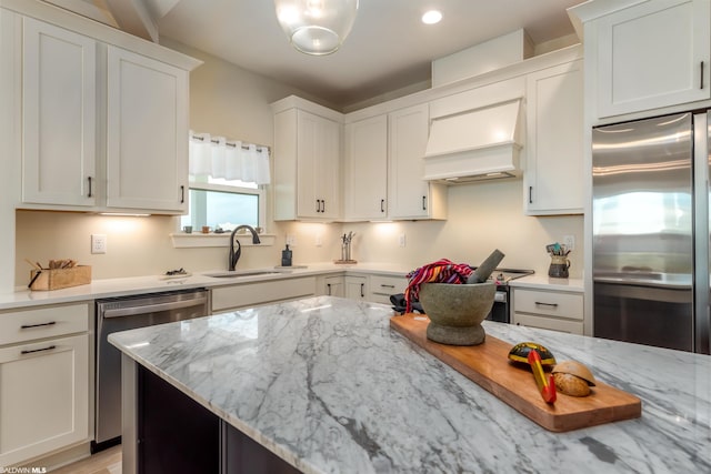 kitchen with stainless steel appliances, custom exhaust hood, white cabinets, light stone counters, and sink