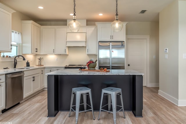 kitchen featuring appliances with stainless steel finishes, light hardwood / wood-style floors, premium range hood, a center island, and light stone counters