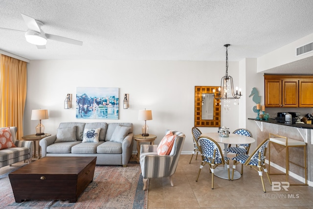living area with a chandelier, light tile patterned floors, a textured ceiling, baseboards, and ceiling fan