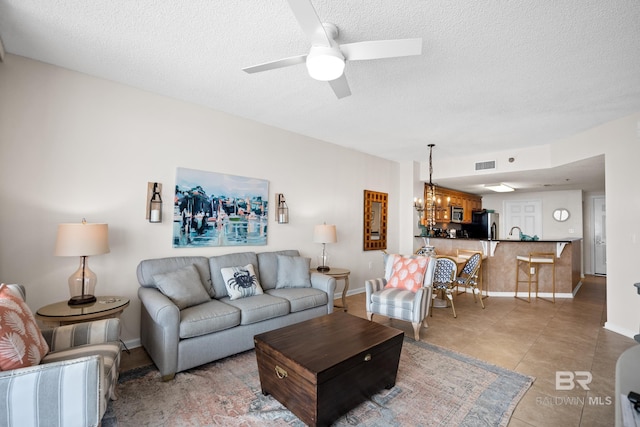 living area featuring a chandelier, baseboards, a ceiling fan, a textured ceiling, and light tile patterned flooring