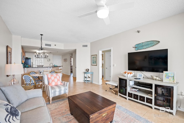 living area featuring a chandelier, light tile patterned floors, a ceiling fan, and a textured ceiling