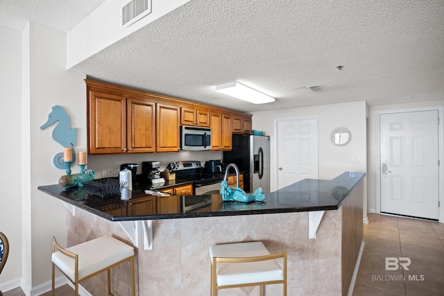 kitchen with stainless steel appliances, a textured ceiling, brown cabinets, a kitchen breakfast bar, and a peninsula