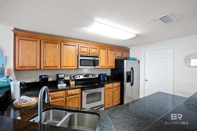 kitchen with stainless steel appliances, a sink, brown cabinetry, and a textured ceiling