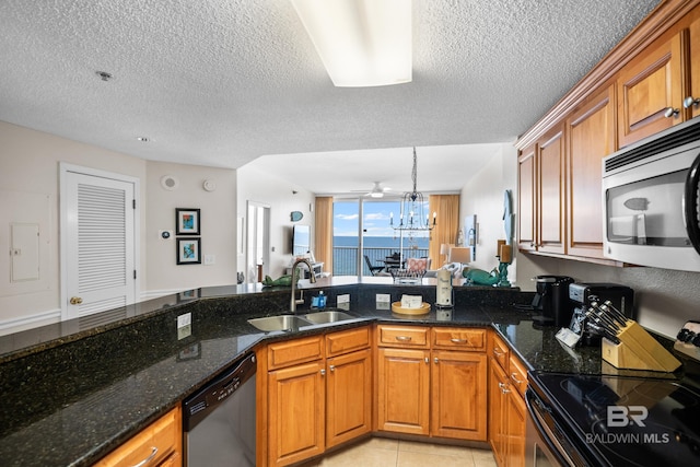 kitchen featuring stainless steel appliances, a sink, brown cabinets, dark stone counters, and a textured ceiling