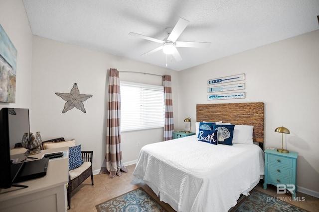bedroom featuring baseboards, ceiling fan, light tile patterned flooring, a textured ceiling, and a desk