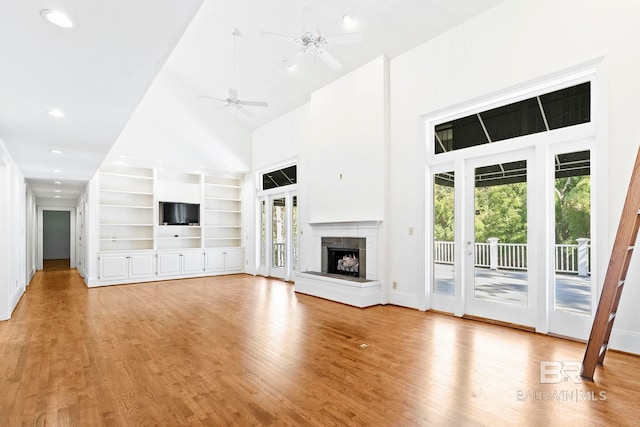 unfurnished living room featuring built in shelves, ceiling fan, high vaulted ceiling, and light hardwood / wood-style flooring