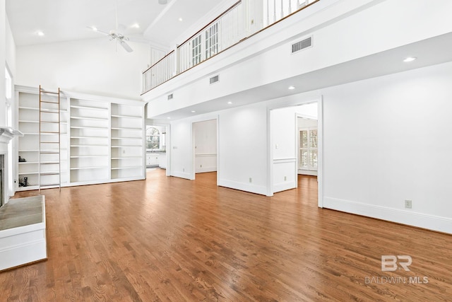 unfurnished living room with ceiling fan, a towering ceiling, and wood-type flooring