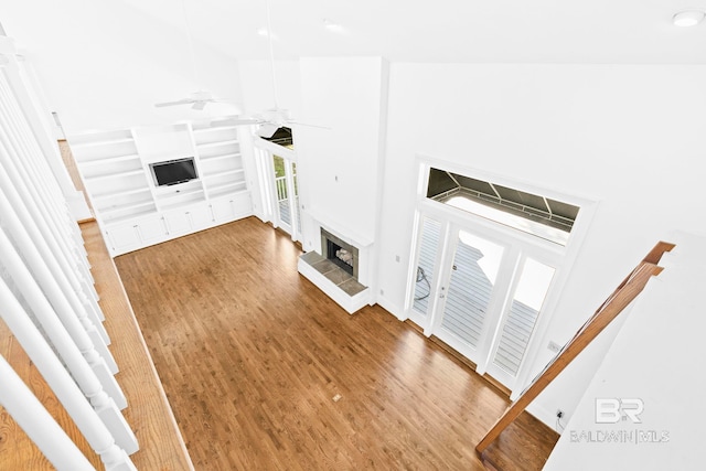 unfurnished living room with a high ceiling, hardwood / wood-style flooring, built in shelves, ceiling fan, and a tiled fireplace