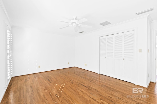 unfurnished bedroom with a closet, hardwood / wood-style flooring, ceiling fan, and crown molding