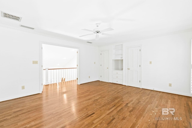 empty room featuring built in shelves, ceiling fan, light hardwood / wood-style floors, and crown molding