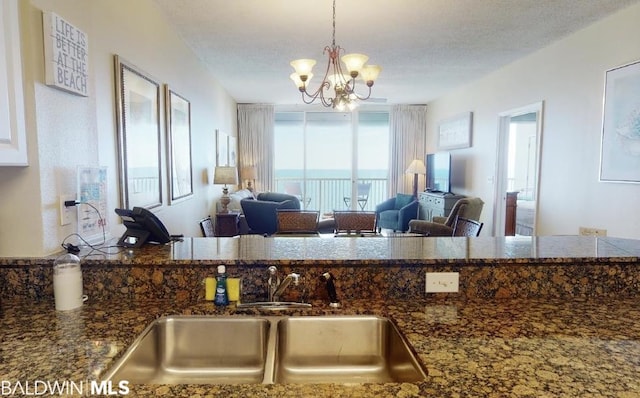 kitchen featuring a textured ceiling, a notable chandelier, dark stone countertops, and sink