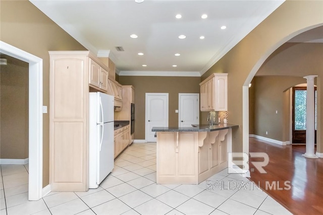 kitchen with white refrigerator, kitchen peninsula, light tile patterned floors, and decorative columns