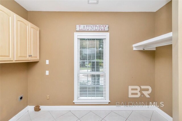 laundry area featuring electric dryer hookup, light tile patterned floors, and cabinets