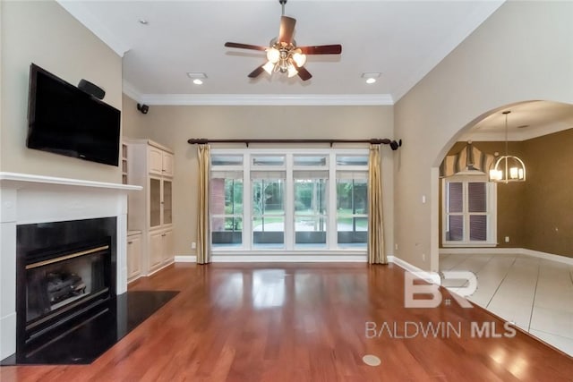 unfurnished living room featuring ornamental molding, ceiling fan with notable chandelier, and light hardwood / wood-style floors