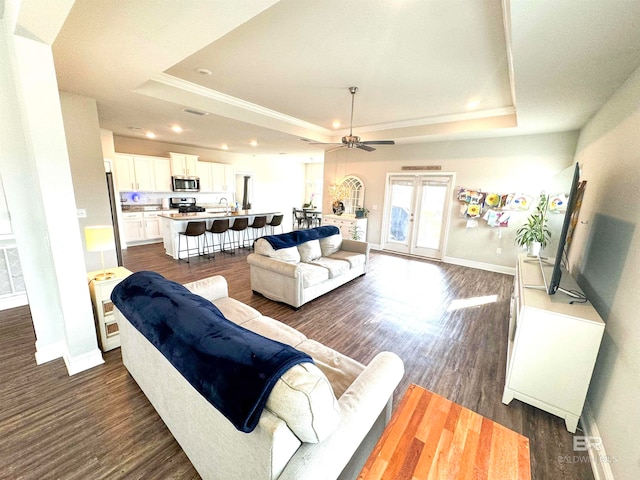 living room featuring ceiling fan, sink, a tray ceiling, and dark hardwood / wood-style flooring