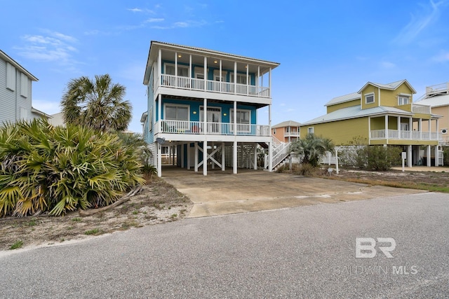 raised beach house featuring a balcony, covered porch, driveway, and a carport