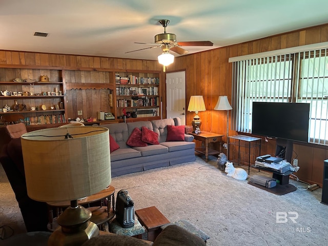 carpeted living room with wooden walls, built in features, and ceiling fan