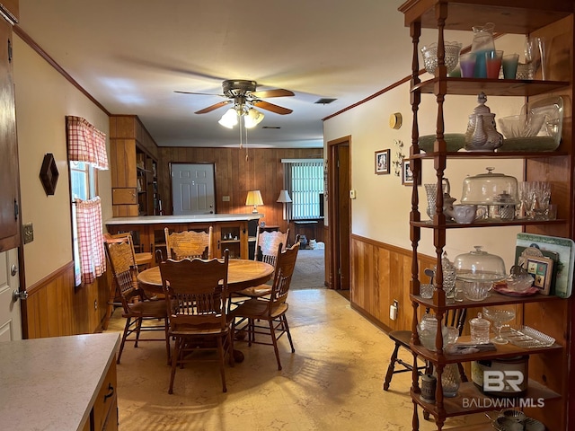 dining area with wooden walls, plenty of natural light, ceiling fan, and crown molding