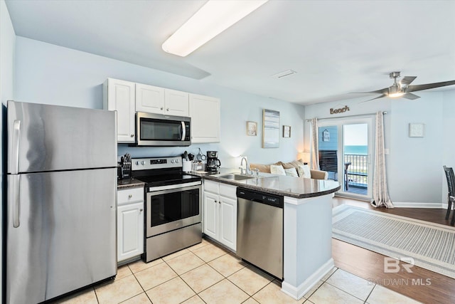 kitchen featuring dark countertops, a peninsula, light tile patterned flooring, stainless steel appliances, and a sink