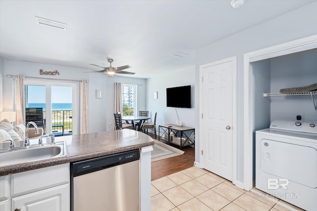 kitchen with light tile patterned floors, washer / dryer, a sink, dishwasher, and dark countertops