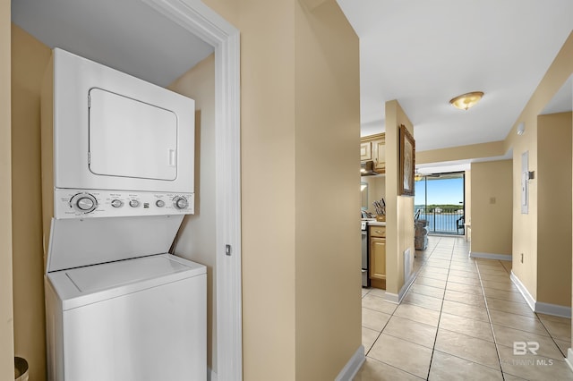 laundry area with light tile patterned floors, laundry area, stacked washer and clothes dryer, and baseboards