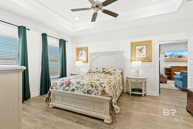 bedroom with ceiling fan, light hardwood / wood-style floors, a tray ceiling, and multiple windows