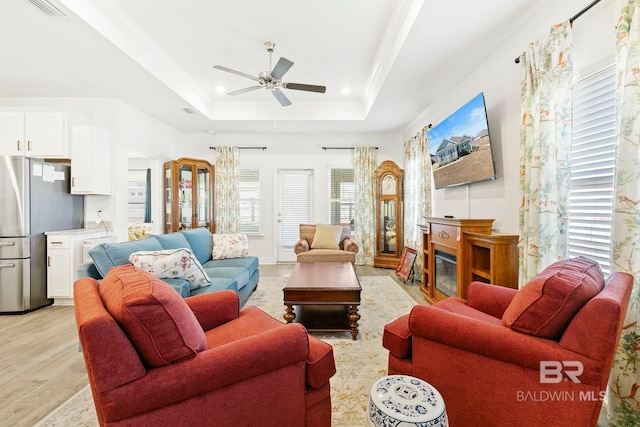 living room with ceiling fan, crown molding, a raised ceiling, and light wood-type flooring