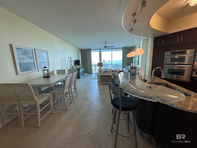 kitchen with pendant lighting, dark brown cabinets, floor to ceiling windows, light stone counters, and stainless steel double oven