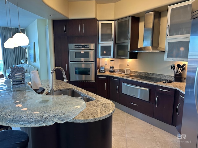 kitchen with sink, double oven, dark brown cabinets, light stone countertops, and wall chimney exhaust hood