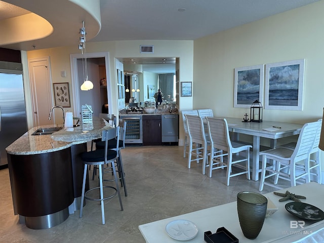 kitchen with pendant lighting, sink, beverage cooler, built in refrigerator, and light stone counters