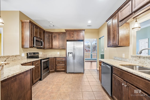 kitchen featuring light stone counters, dark brown cabinetry, stainless steel appliances, sink, and decorative light fixtures